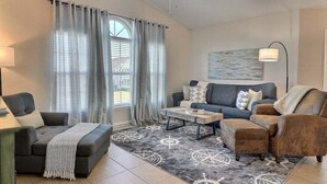 A living room with a sofa, armchair, and ottoman, a coffee table, and a rug with a nautical theme. - 2BR Condo | mins to Beach & Sports Complex (Gulf Shores)