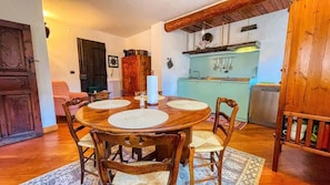A dining area with a wooden table and chairs, a kitchen in the background, and a rustic wooden door.