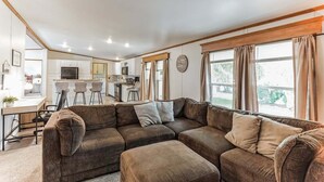 Ein modernes Wohnzimmer mit einem Ecksofa, einem Essbereich und einer Küche im Hintergrund.