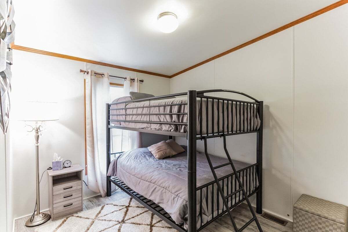 Een slaapkamer met een stapelbed, een nachtkastje, een vloerlamp en een klein nachtkastje-lade.