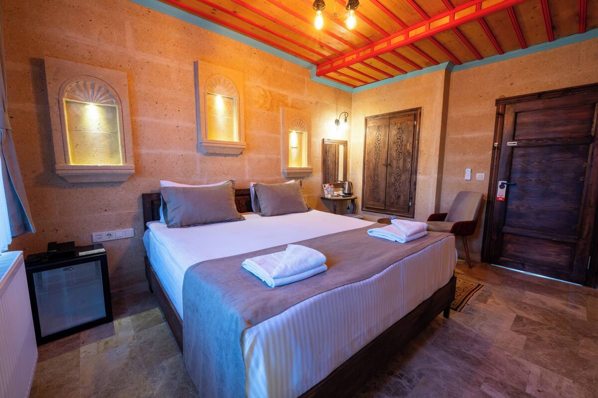 A hotel room with a large bed, bedside tables, a small refrigerator, and a wooden door.