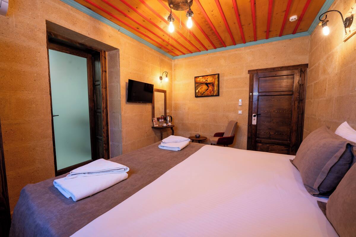 A hotel room with a large bed, a flat-screen TV, a wooden door, and a small table with a chair.
