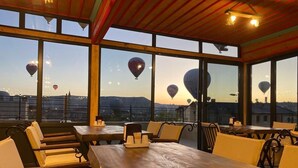 A restaurant with a large wooden table and yellow chairs, large windows with a view of hot air balloons. - Rustic Caves (Nevsehir)