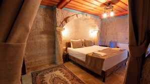 Ein Schlafzimmer mit Steinsandsteinwand, Holzbalkendecke, einem Bett mit Holz Kopfteil, einem Nachttisch und einem gemusterten Teppich.