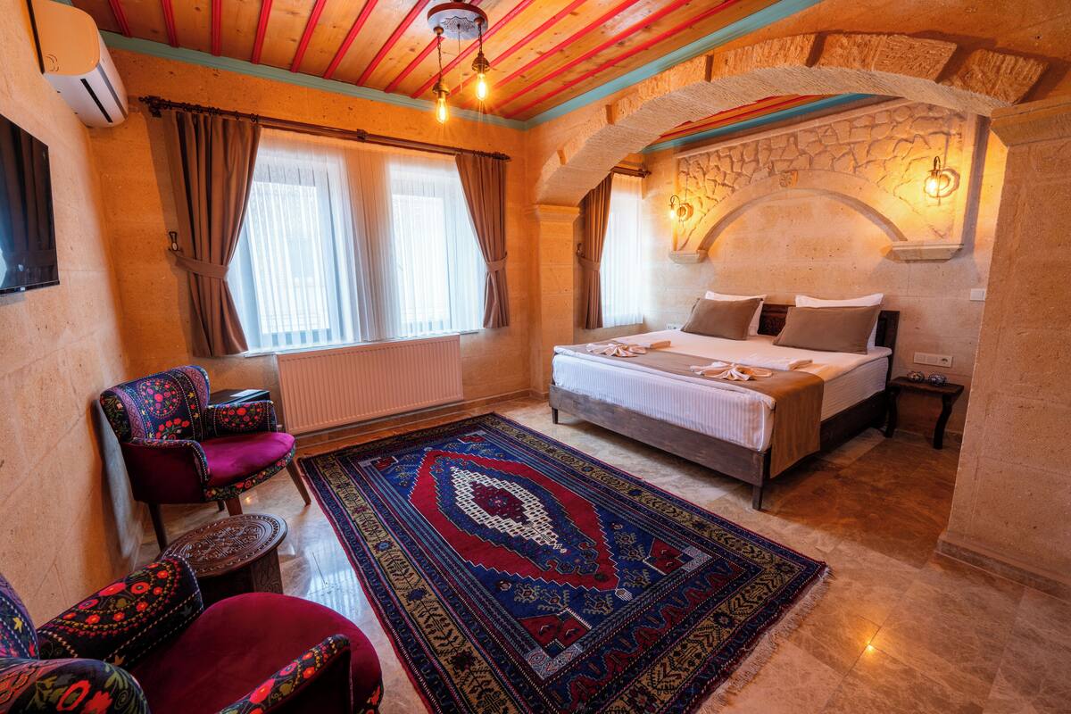 A cozy bedroom with a bed, a chair, a rug, and a stone wall.