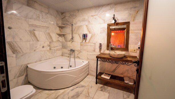 A bathroom with a large freestanding bathtub, a toilet, a vanity with a mirror, and marble walls. - Rustic Caves (Nevsehir)
