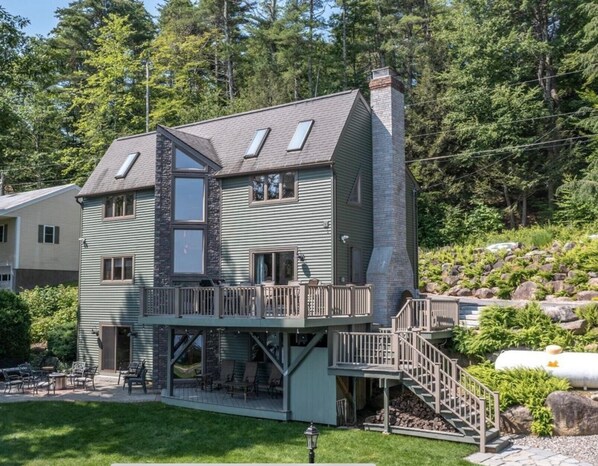 A two-story house with a balcony and a deck, surrounded by a wooded area.