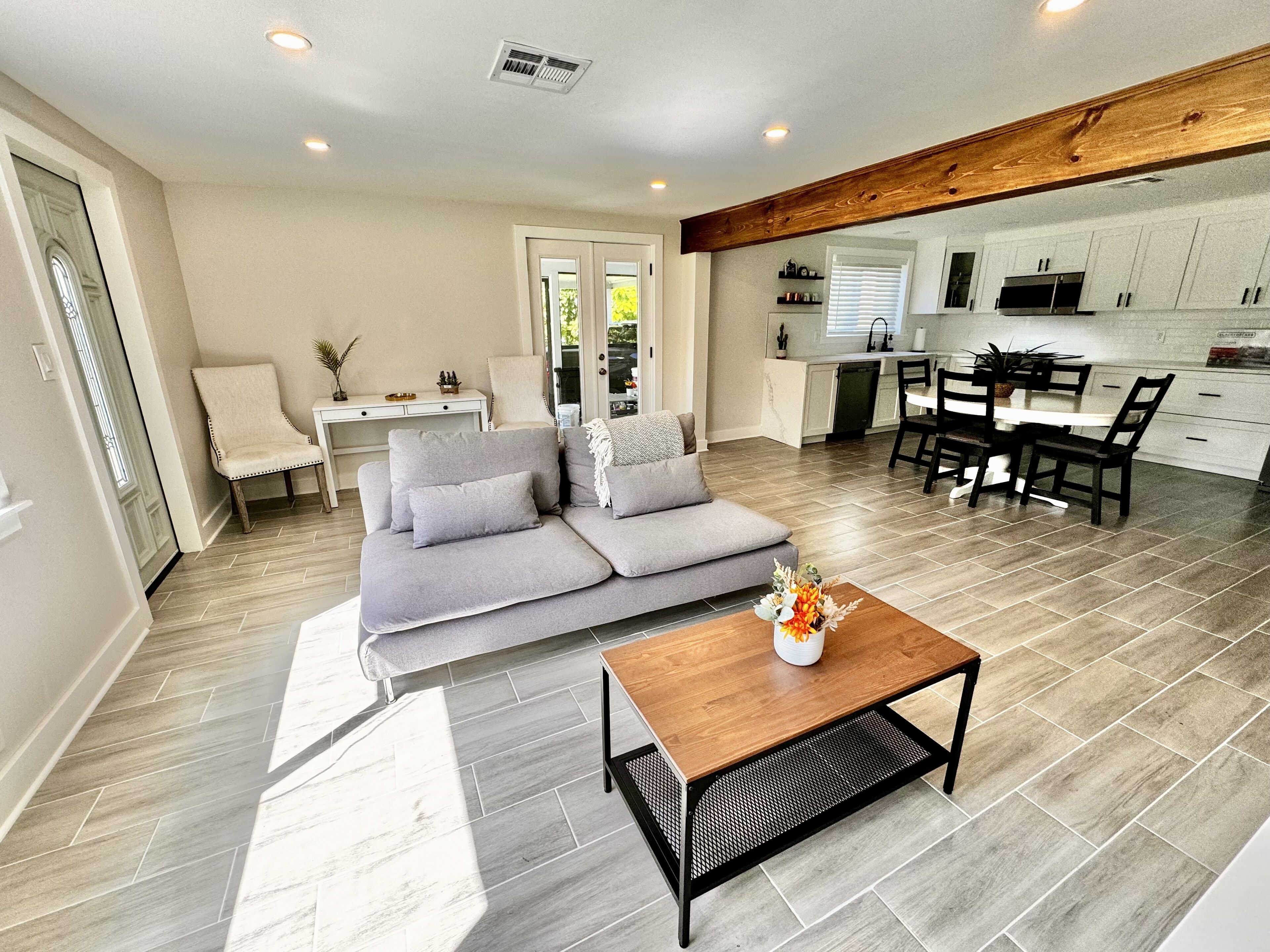A modern living room with a grey sectional sofa, a wooden coffee table, and a dining area with a black table and chairs.