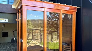 A wooden structure with glass doors, a metal railing, and a view of a natural landscape. - NEW 4BD, 4BA, Sleeps 13, Close to Ski Lifts, Sauna, Mtn Views (Angel Fire)