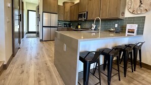A modern kitchen with wooden cabinets, a stainless steel refrigerator, a microwave, and a large island with bar stools. - NEW 4BD, 4BA, Sleeps 13, Close to Ski Lifts, Sauna, Mtn Views (Angel Fire)
