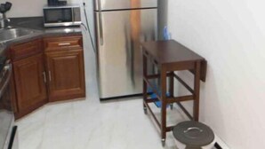 Une cuisine compacte avec des meubles en bois, un réfrigérateur en acier inoxydable, un four à micro-ondes et une petite table en bois.