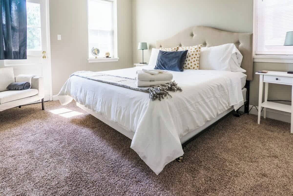 A neatly arranged bedroom with a large bed, a bedside table, a lamp, and a window with curtains.