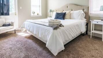 A neatly arranged bedroom with a large bed, a bedside table, a lamp, and a window with curtains.