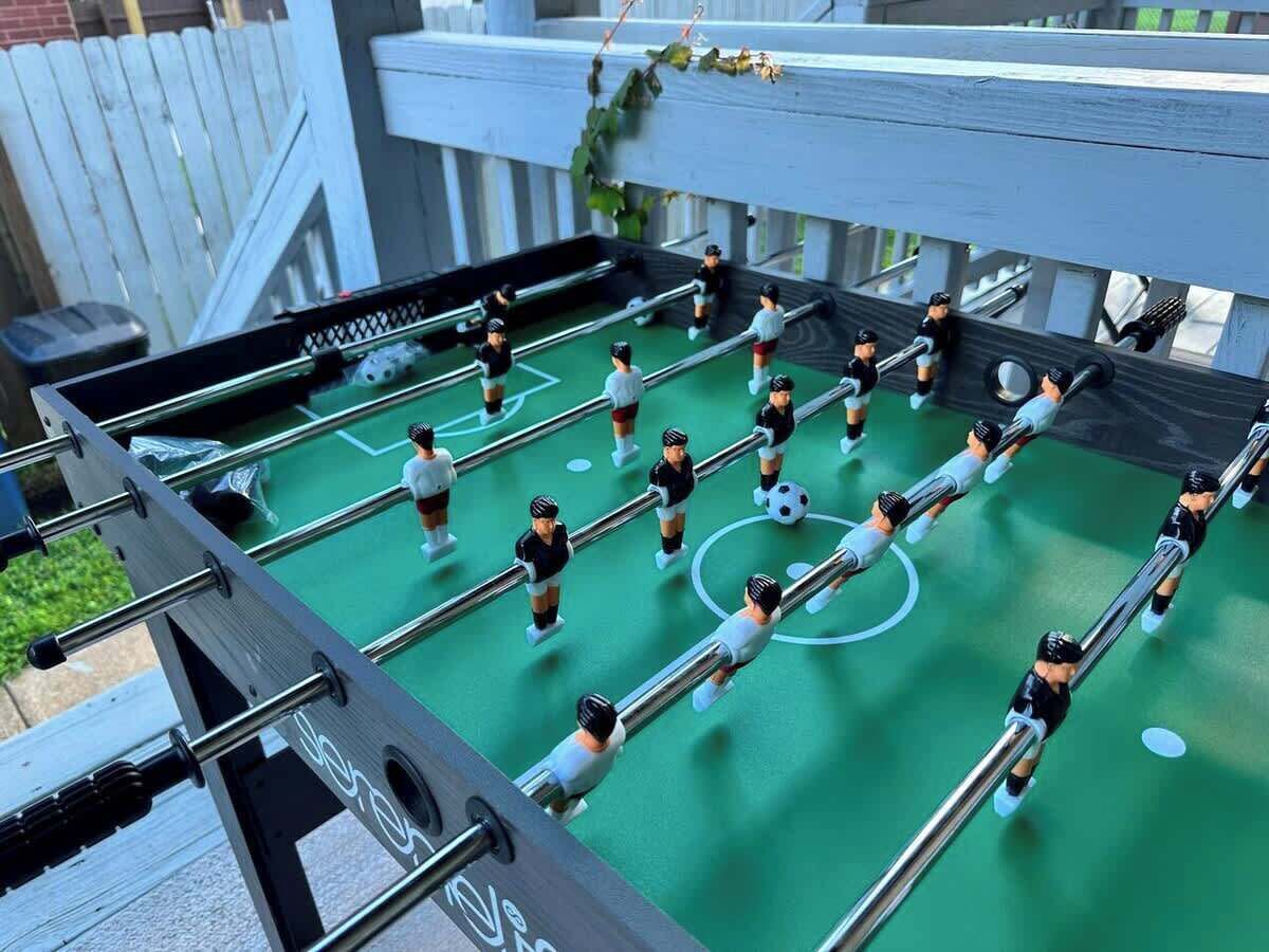 Un juego de mesa con figuras en miniatura y una pelota de fútbol sobre un tablero verde.