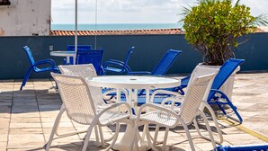 Una terraza con una mesa redonda y sillas, una planta en maceta y vista al mar.