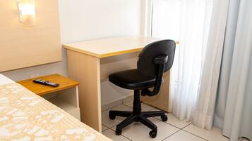 Een hotelkamer met een bed, een bureau, een stoel, een afstandsbediening en een raam met gordijnen.