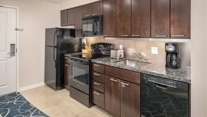 Una cocina compacta con armarios de madera oscura, un refrigerador de acero inoxidable, un microondas, una estufa y un lavavajillas.