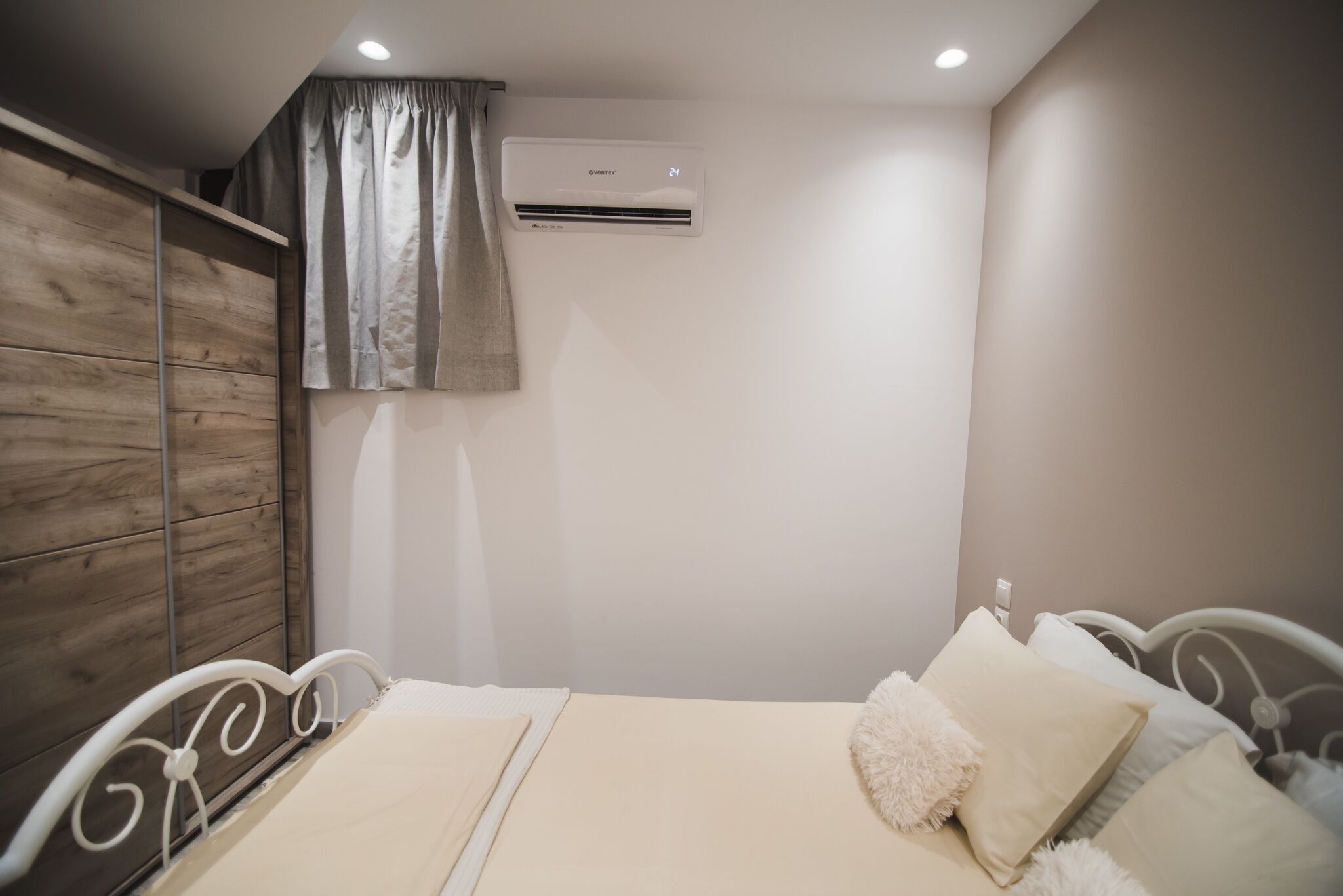 A bedroom with a bed, a wardrobe, an air conditioning unit, and a curtain.