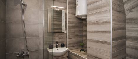 A modern bathroom with a shower, sink, and a small potted plant.