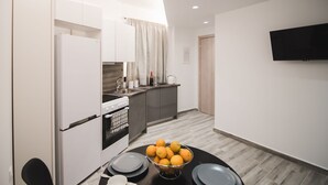 A modern kitchen with white cabinets, a black refrigerator, and a dining table with a bowl of oranges. - Contemporary Studios Historic Center (Corfu)