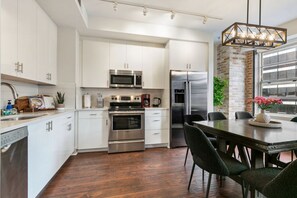 Una cocina moderna con armarios blancos, electrodomésticos de acero inoxidable y un comedor con mesa y sillas.