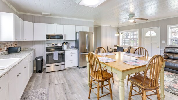 A modern kitchen with white cabinets, stainless steel appliances, and a dining area with wooden chairs and a table. - 2 Mi to Mashes Sands Beach: Quiet Home w/ Dock! (Panacea)
