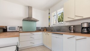 A modern kitchen with white cabinets, a dishwasher, a coffee maker, and a window with a view of trees. - Ô Soleil - Avec piscine privée (Vendres)