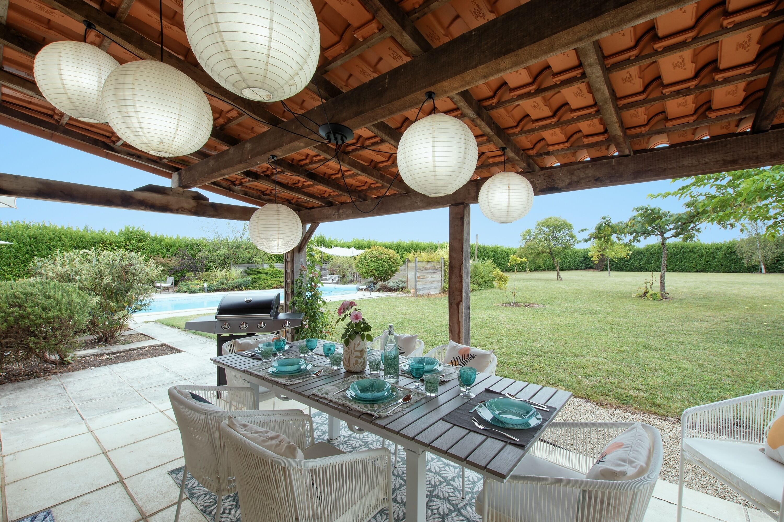 An outdoor patio with a wooden pergola, white wicker furniture, and a dining table set with blue and white dinnerware.