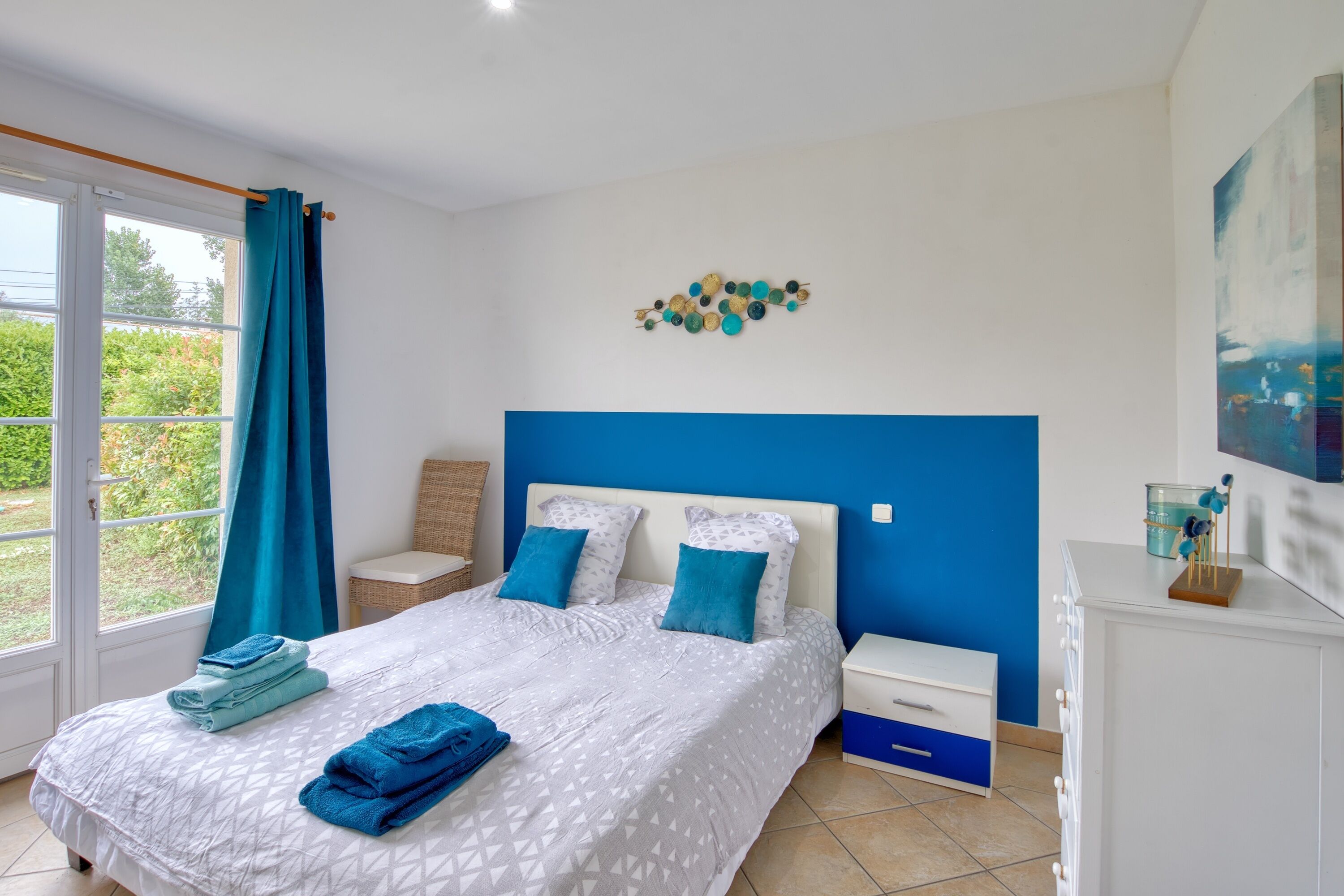 Une chambre à coucher avec un lit, des tables de chevet, une commode et une fenêtre avec des rideaux.