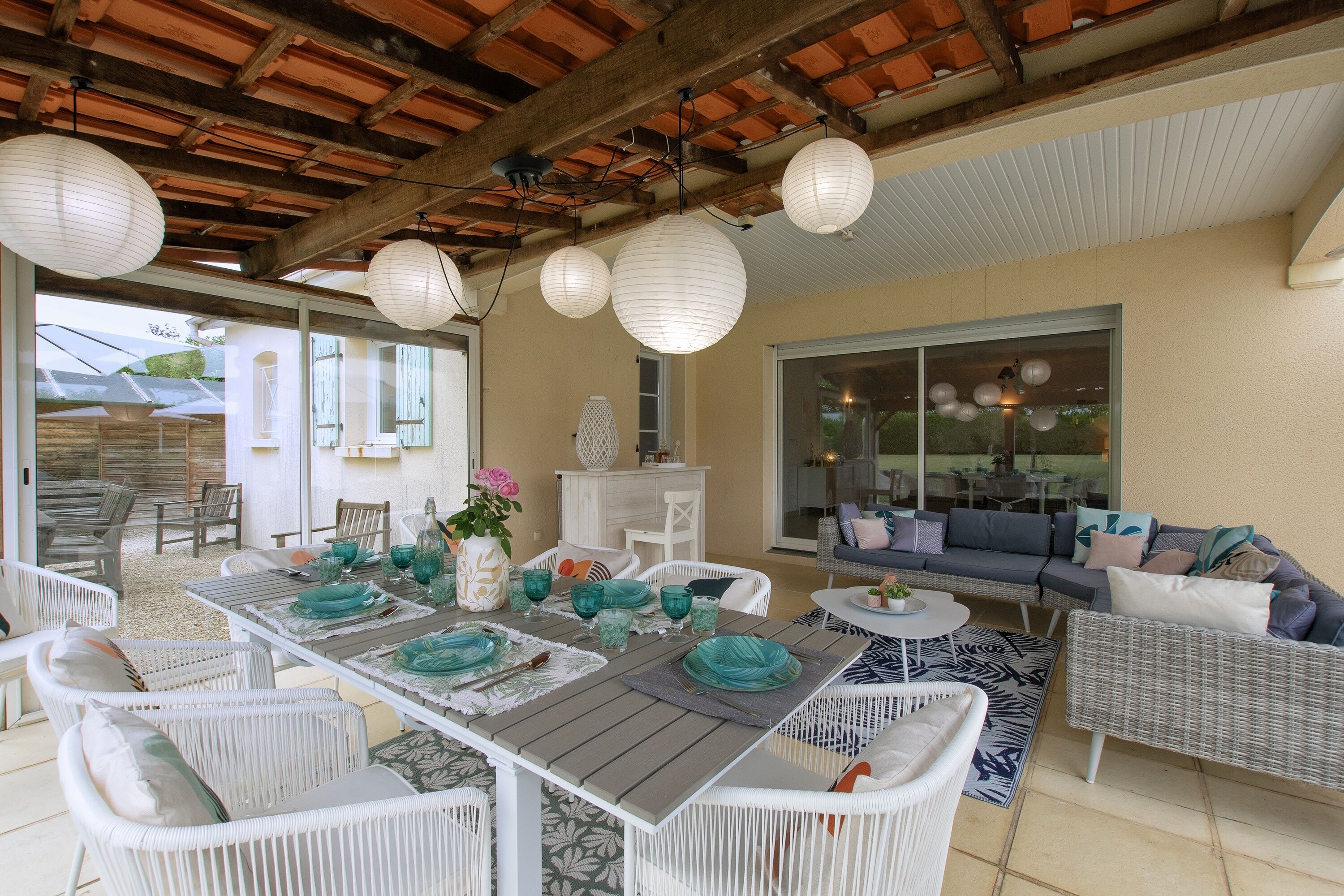 An outdoor patio with a wooden table set for dining, surrounded by wicker chairs and a sofa.