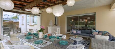An outdoor patio with a wooden table set for dining, surrounded by wicker chairs and a sofa.
