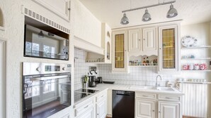 A modern kitchen with white cabinetry, stainless steel appliances, and a black dishwasher. - La Maison des Sources - A 20min du Puy du Fou (Mortagne-sur-Sèvre)
