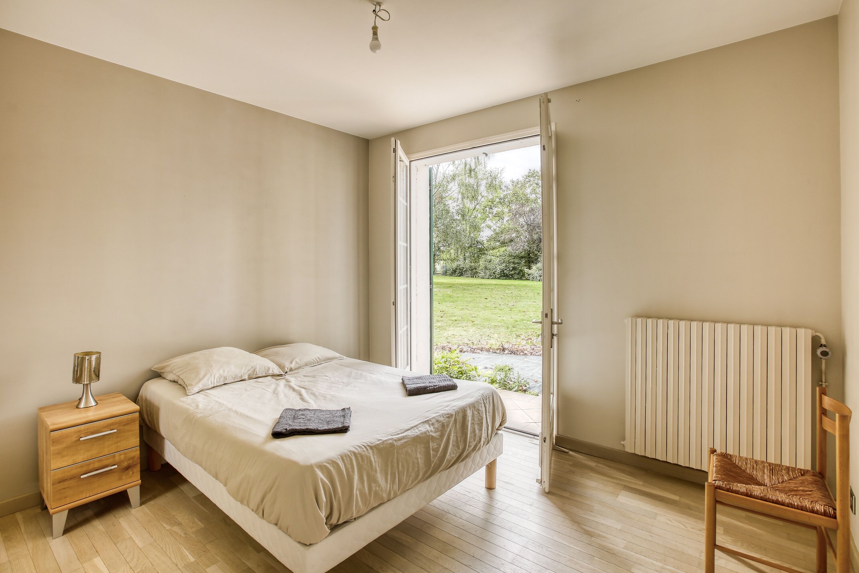 Un dormitorio con una cama, una mesita de noche, una silla y vistas al exterior.