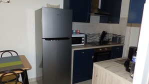 A compact kitchen with a stainless steel refrigerator, a microwave, and a toaster. There is a wooden dining table with chairs and a small cabinet.