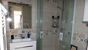 A bathroom with a glass-enclosed shower, a sink with a mirror, and a tiled backsplash.