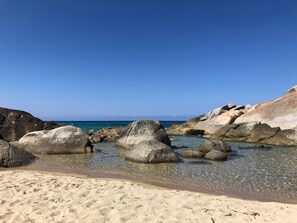 Une plage avec de gros rochers et une eau d’un bleu limpide.