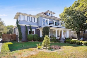 A two-story house with a covered porch, a small front yard with a tree, and a wooden fence.