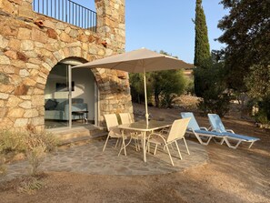 Un bâtiment en pierre avec une porte en verre donnant sur un espace aménagé avec une table, des chaises et un parasol.