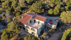 Un edifici de pedra de dos pisos amb teulada vermella, un balcó i un cotxe a l'exterior.