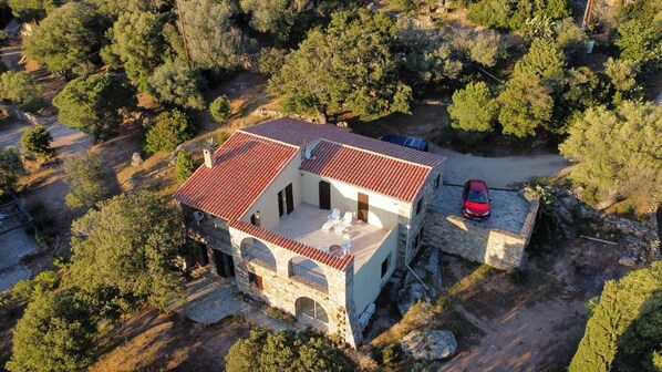 Un bâtiment en pierre de deux étages, avec un toit recouvert de tuiles rouges, un balcon et une voiture garée à l’extérieur.