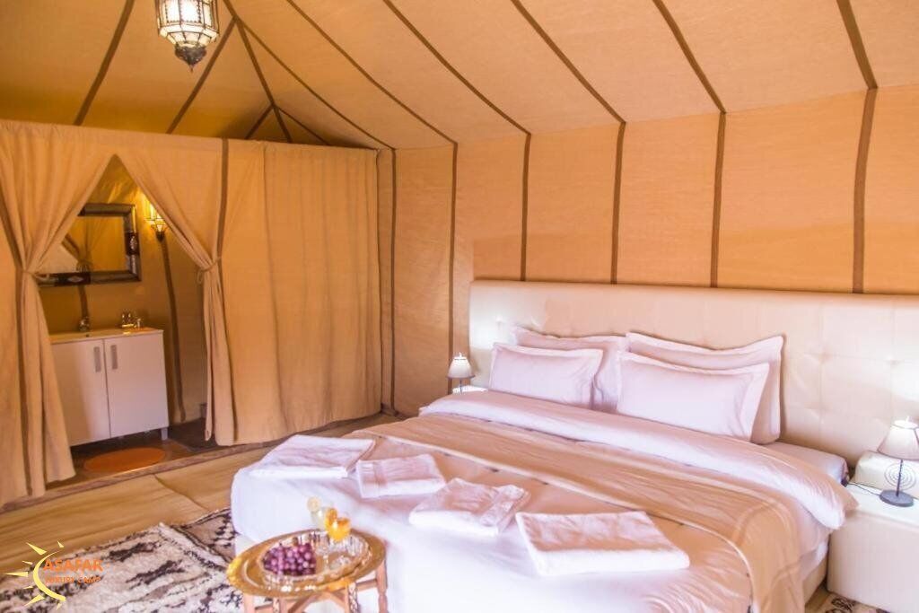 A bedroom with a large bed, a nightstand, a mirror, and a small table with a tray.
