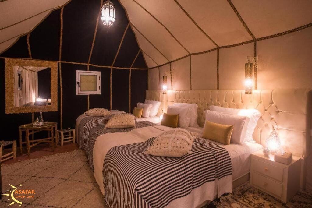 A tented luxury camp room with two beds, bedside tables, and a mirror.