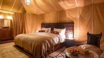 Una habitación con tienda de campaña, una cama grande, una mesita de noche con lámpara y una pequeña mesa con frutas.