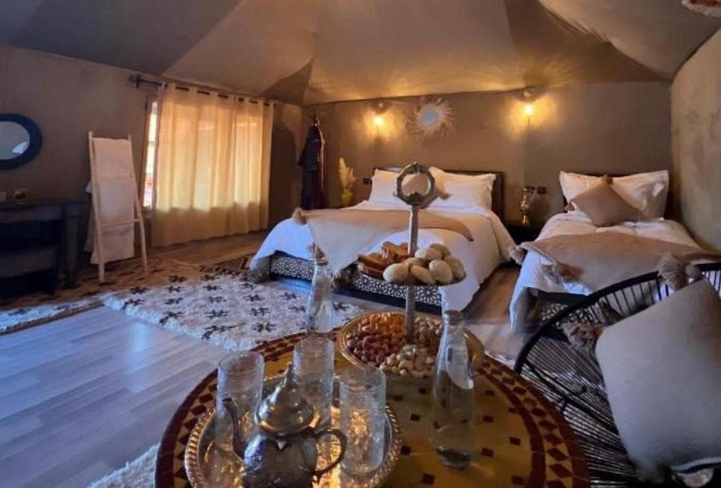 A cozy bedroom with a bed, a side table, a tray with glasses and snacks, and a decorative mirror.