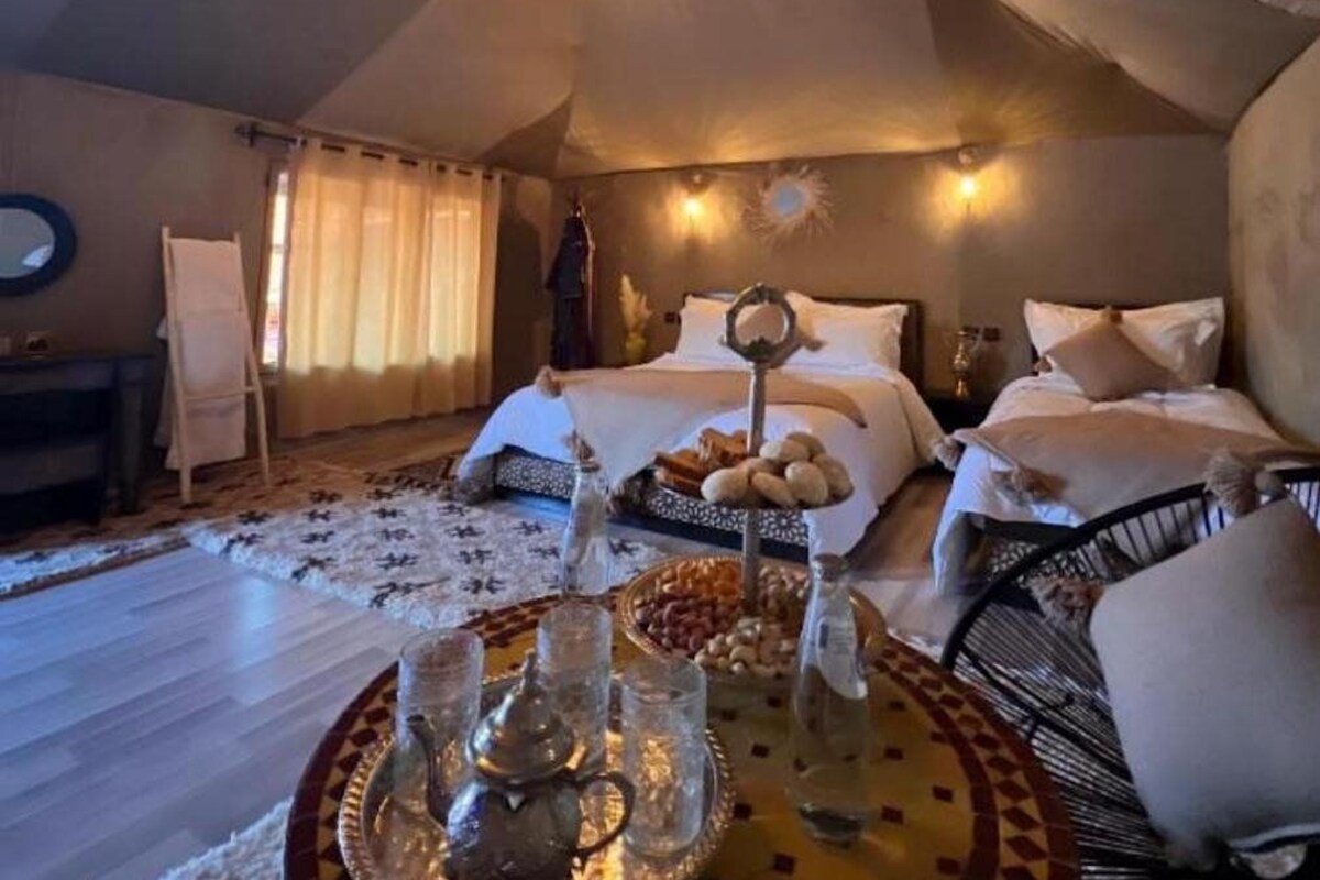Um quarto aconchegante com uma cama, uma mesinha de cabeceira, um tabuleiro com copos e petiscos, e um espelho decorativo.