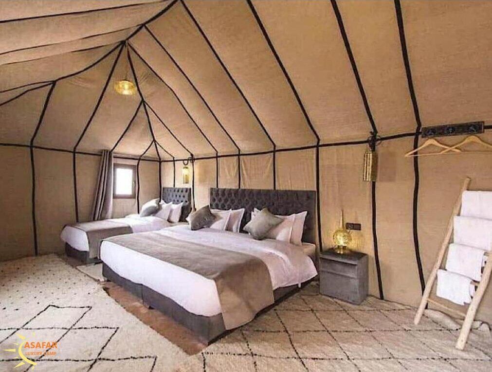 A tented room with two beds, a bedside table with a lamp, and a hanging clothes rack.