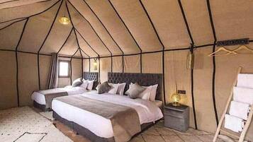 A tented room with two beds, a bedside table with a lamp, and a hanging clothes rack.
