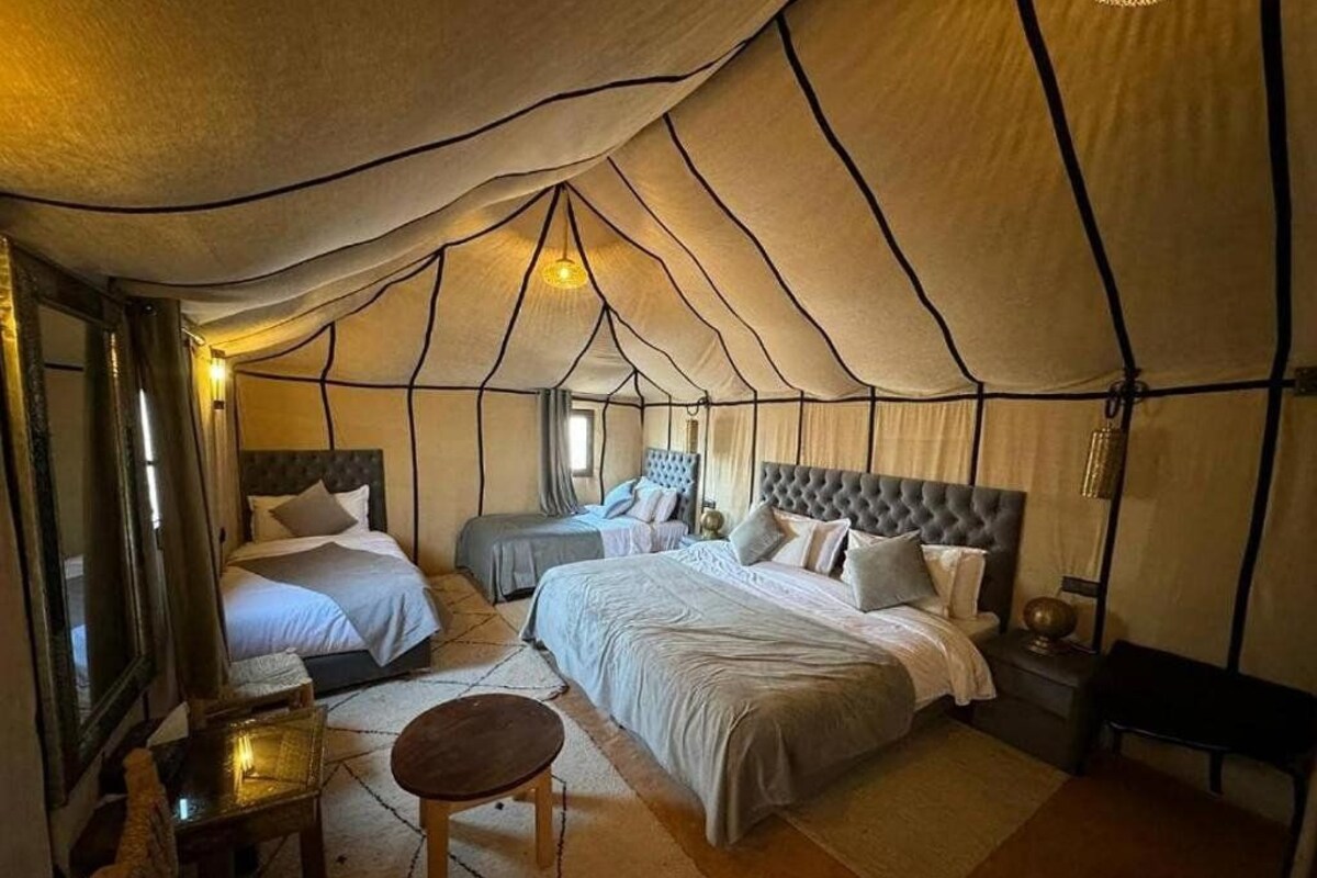 A tented luxury camp room with two beds, a small table, and a bench.