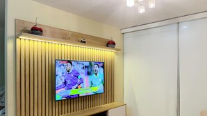Ein an der Wand befestigter Fernseher mit Holzpaneeloptik, darüber ein Regal und eine Deckenleuchte.