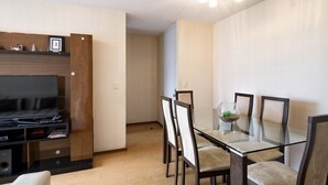 Ein modernes Wohnzimmer mit Flachbildfernseher, Holz-Unterhaltungseinrichtung und einem Glastisch mit vier Stühlen.